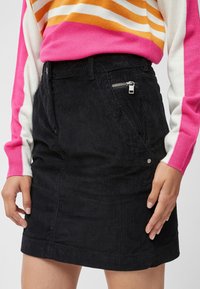 Sort corduroykjole med en tætsiddende design, der har sidelukninger og lommer. Teksturen er ribbet, og kanten er lige.