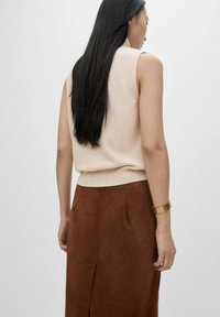 Beige mouwloze trui met een geribbelde zoom, gecombineerd met een bruine suède rok met zijzakken en een split aan de voorkant. Accents met een armband in goudkleur.