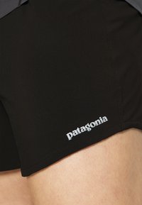 Calções atléticos pretos com uma textura suave, apresentando um logo branco "Patagonia" na bainha. Design limpo e forma ajustada.