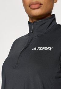 Fekete cipzáras dzseki magas gallérral és finom textúrával, a mellrészen fehér "TERREX" logóval.