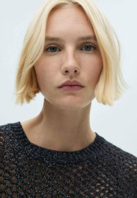 Top nero lavorato a maglia con motivo aperto, scollatura tonda e finitura testurizzata. La modella ha i capelli biondi corti e un trucco naturale.
