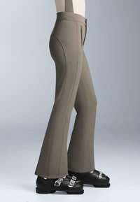 Pantaloni svasati color cachi con una texture liscia, dettagli di cuciture visibili e una vita alta, abbinati a stivali da sci neri con fibbie metalliche.