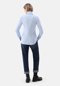 Long-sleeved light blue shirt with a collar, paired with rolled-cuff dark blue jeans and black ankle boots. Simple design, smooth texture.