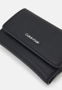 Čierna kožená peňaženka s textúrovaným povrchom, na prednej strane so strieborným logom Calvin Klein a so zapínaním na preloženie.