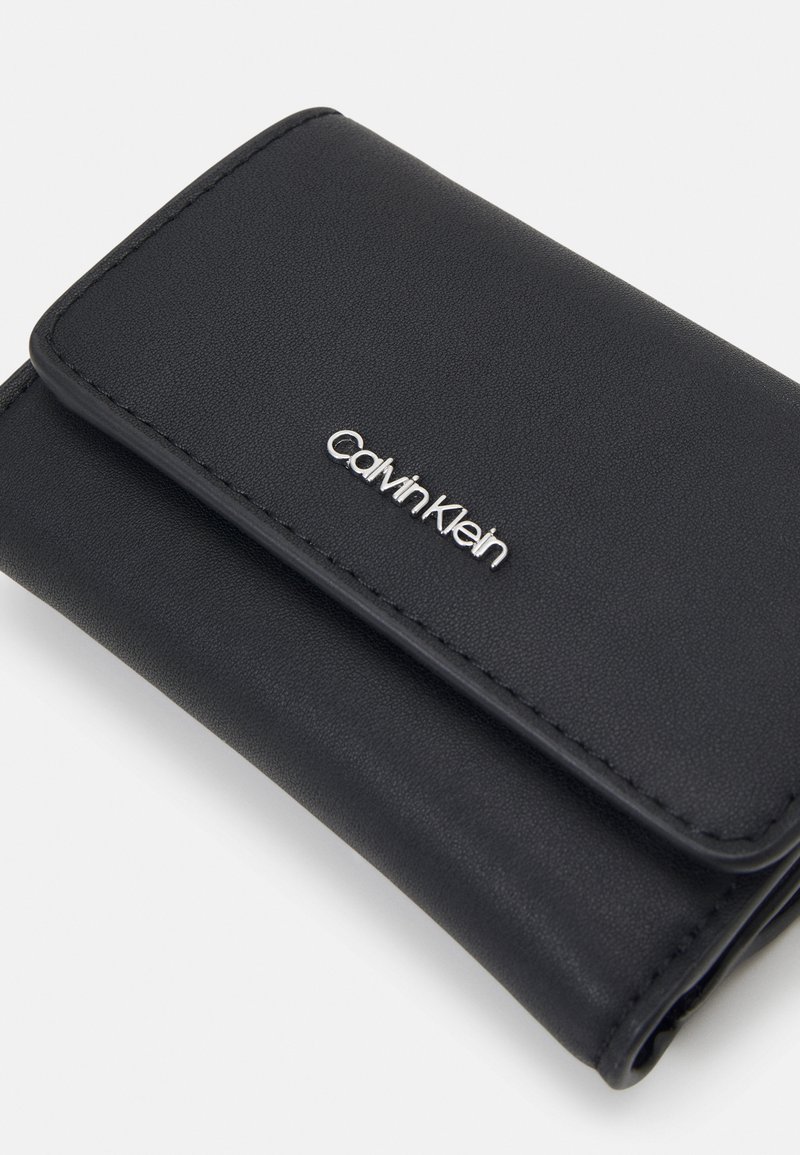 Schwarze Lederbörse mit strukturierter Oberfläche, ausgestattet mit einem silbernen Calvin Klein-Logo auf der Vorderseite und einem Klappverschluss.