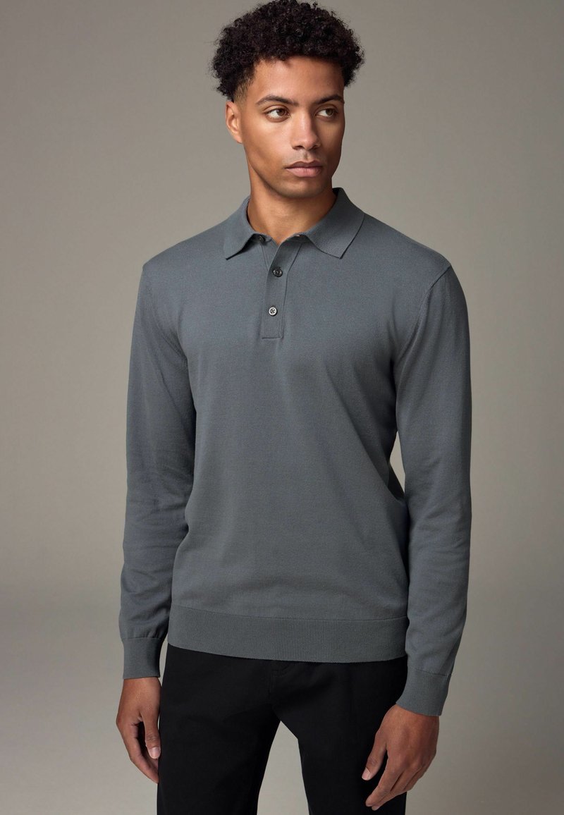 Langärmliges Poloshirt aus dunkelgrauer Baumwolle mit Kragen, Drei-Knopf-Leiste sowie gerippten Bündchen und Saum. Das Modell steht vor einem neutralen Hintergrund.