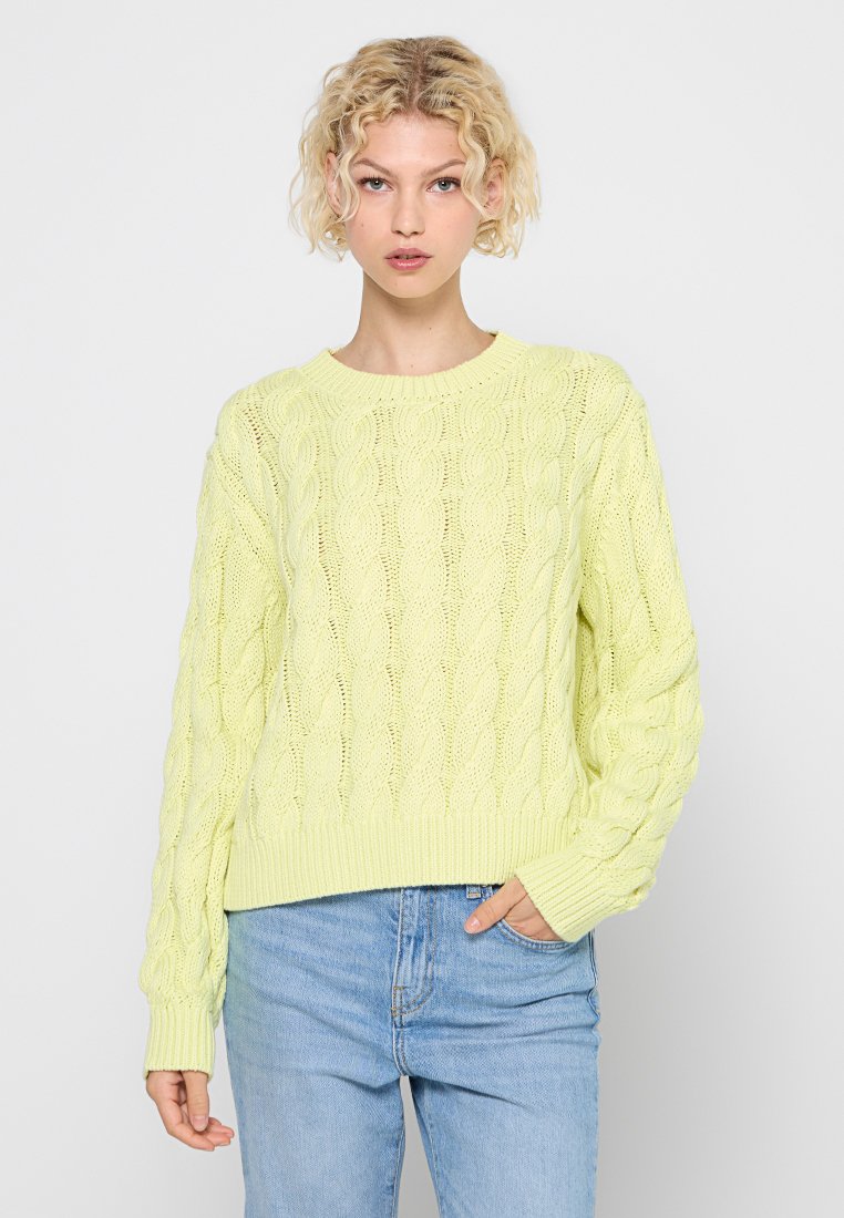 Pull en maille torsadée jaune clair avec un col rond, un ourlet côtelé et des manches légèrement surdimensionnées, associé à un jean en denim.