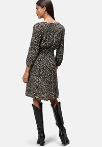 Robe noire à motifs floraux avec des manches longues, une taille cintrée et une jupe évasée, associée à des bottes noires jusqu'aux genoux. Tissu doux et fluide.