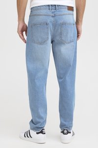 Pantalones vaqueros de mezclilla azul claro con un corte relajado, que cuentan con dos bolsillos traseros y un parche de cuero en la cintura. Se combinan con zapatillas blancas.