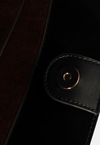 Schwarze Ledertasche mit einem dunkelbraunen Wildlederpanel. Akzentuiert mit einem goldfarbigen Druckknopf und eleganten Nähte.