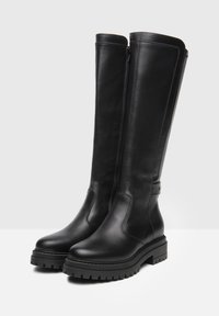 Bottes en cuir noir montantes avec une semelle épaisse, fermeture éclair sur le côté et texture lisse. Présente un design minimaliste et une construction durable.