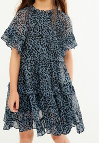 Sininen leopardikuvioinen mekko läpinäkyvässä kankaassa, jossa on rypytetyt lyhyet hihat ja kerroksittaisia osia. Herkkä tekstuuri ja virtaava muotoilu.
