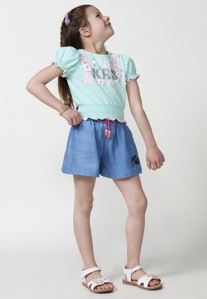 Haut bleu clair à manches courtes avec broderie florale et taille smockée, associé à un short en denim avec un accent brodé et un cordon de serrage rose.