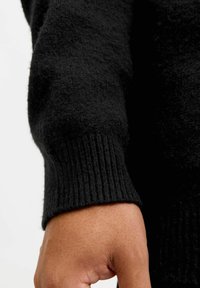 Czarny dziany sweter z bliska, prezentujący teksturowany materiał, ściągacz na rękawach oraz gładką powierzchnię bez widocznych wzorów czy akcentów.