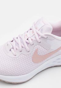 Svijetlo ružičasta atletska cipela s teksturiranim mrežastim gornjištem, mekanim vezicama, potpisanim rose gold swooshom i bijelim potplatom.