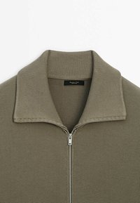 Olijfgroene trui met ritssluiting en geribde kraag, gemaakt van een textuurgebreide stof. Voorzien van een metalen rits en een label aan de binnenkant van de kraag.