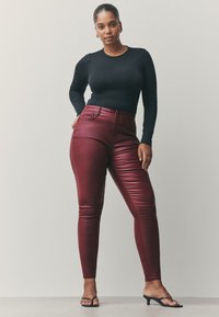 Črna majica z dolgimi rokavi v kombinaciji z ozkimi bordo umetno usnjenimi hlačami z visokim pasom. Model nosi črne sandale s peto.