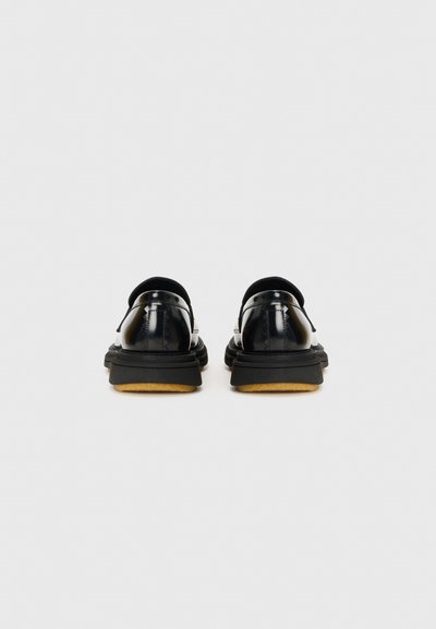 Chaussures en cuir verni noir avec une semelle épaisse noire et une semelle intérieure en cuir souple marron, dotées de talons arrondis et d'un minimalisme dans les détails.