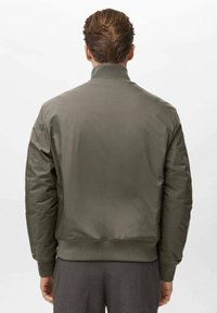 Chaqueta bomber verde oliva con cuello alto, puños acanalados y un acabado suave y texturado. Presenta un dobladillo recto y sin hardware visible.