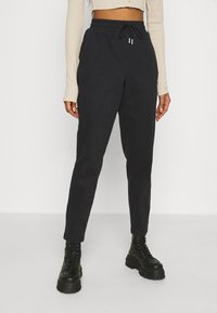 Czarne zwężane joggery z elastycznym pasem, zaciąganym sznurkiem i bocznymi kieszeniami, zestawione z masywnymi czarnymi butami na sznurówki.