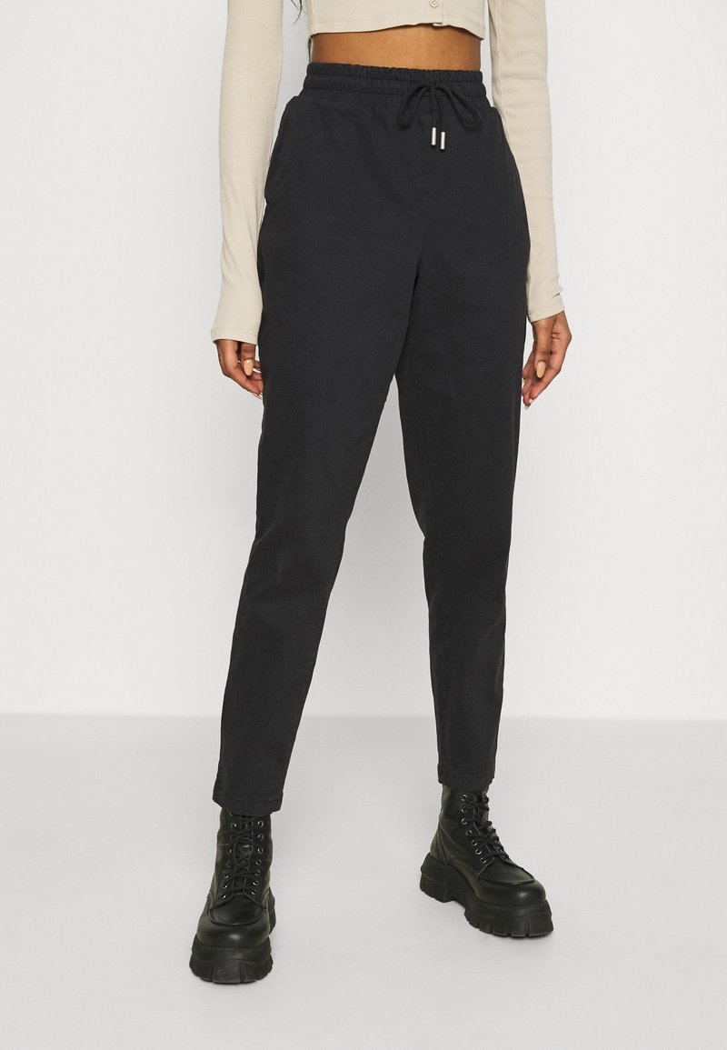 Czarne zwężane joggery z elastycznym pasem, zaciąganym sznurkiem i bocznymi kieszeniami, zestawione z masywnymi czarnymi butami na sznurówki.