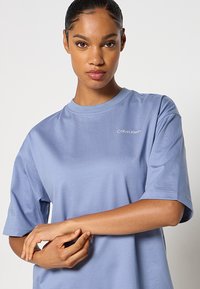 Jasnoniebieska koszulka z krótkim rękawem wykonana z gładkiego bawełnianego materiału. Posiada okrągły dekolt i małe białe logo Calvin Klein na piersi.