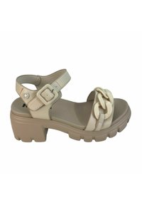 Sandal de plataforma beige con un grueso tacón cuadrado, que presenta una correa en el tobillo ajustable y una cadena decorativa en el empeine. Textura suave.