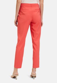 Koralowe, dopasowane spodnie o prostym kroju, gładkiej fakturze i tylnych kieszeniach. Noszone z jasnymi, odkrytymi butami.