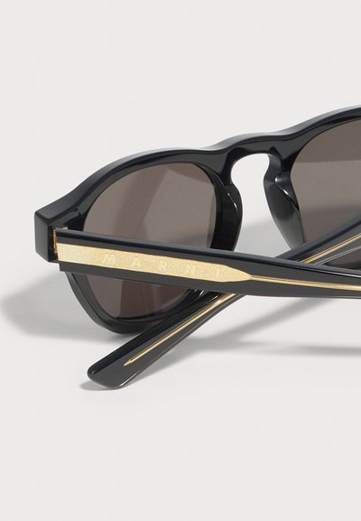 Schwarze Cat-Eye-Sonnenbrille mit dunklen Gläsern und goldakzentuierten Bügeln, bei einem Bügel ist das "MARNI"-Logo eingraviert.