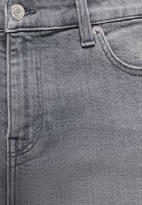 Κοντινή λήψη γκρι τζιν από denim που δείχνει μεταλλικό κουμπί, θηλιά ζώνης, μπροστινή τσέπη και λεπτομέρειες με καρφιά σε υφασμένο ύφασμα.