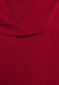Tissu rouge au toucher lisse comportant des plis et des détails drapés, créant un design élégant. La couleur est une teinte rouge profonde et riche.