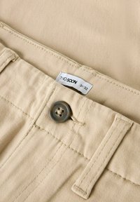 Beige bomullbyxor med framknapp, sydd midja och tygmärke märkt "TWO SOON" storlek 31/32. Slät textur.