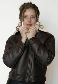 Brun læder bomberjakke med en pelskrave, lange ærmer, lynlåslukning og ribkanter, der viser en blød tekstur og robust design.