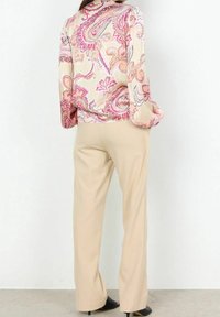 Blouse à manches longues en tissu doux et soyeux, présentant un motif paisley rose et crème, associée à un pantalon tailleur beige clair.