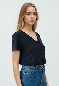 Maglietta nera a maniche corte con scollo a V realizzata in tessuto morbido, abbinata a jeans blu di denim a vita alta con una cintura nera e cuciture delicate.