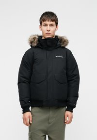 Μαύρο μπουφάν με γούνα στην κουκούλα, με κλειστό μπροστινό μέρος, ελαστικούς καρπούς και δύο μεγάλες μπροστινές τσέπες. Λογότυπο Columbia στο στήθος.