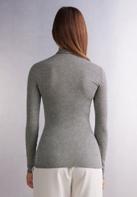 Grå långärmad polotröja med en figurnära silhuett, tillverkad av ett mjukt, texturerat tyg, med sömlösa axlar och smala ärmar.