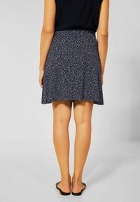 Tmavě modrá sukně s bílými tečkami, měkká látka, zvonový střih. Nošena s sandály, délka do poloviny stehen, elastický pas, bez viditelných zapínání.