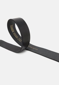 Cinturón negro de cuero genuino hecho en Italia, en forma de lazo para mantenerse erguido sobre un fondo liso y claro con texto dorado en el interior.