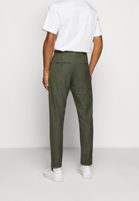 Olivgröna byxor med en tapered ben-design, tillverkade av tyg med en smidig textur, med snedställda fickor och bälteshällor.