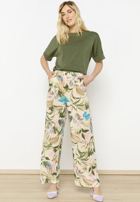 Green short-sleeve shirt paired with wide-legged, floral-printed pants featuring teal, pink, and green leaves, worn with light purple shoes.