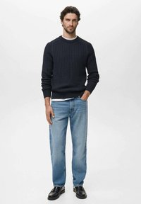 Jersey de punto navy con textura acanalada, combinado con jeans rectos de color azul claro. El modelo lleva zapatos negros. Camiseta blanca lisa visible.