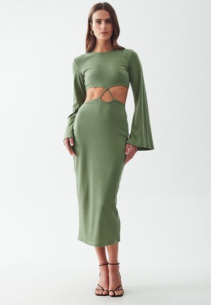 Olive green ribbed knit dress with a cut-out design at the waist, long bell sleeves, and a fitted silhouette, paired with strappy heels.