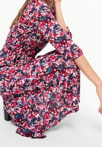 Vestido floral que presenta una mezcla de flores en tonos rosa, rojo y azul sobre un fondo oscuro, con mangas largas y cintura ajustada.