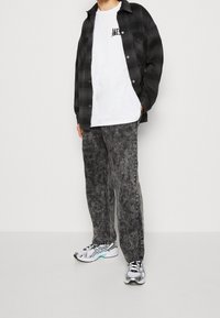 Czarna i szara koszula flanelowa w kratę, biała koszulka z nadrukiem, czarne spodnie o fakturze oraz srebrne sportowe buty z turkusowymi akcentami.