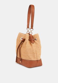 Tan bucket bag med tekstureret vævet finish, læderbund og justerbar skulderrem. Har snøre lukning og hardware i guld tone.