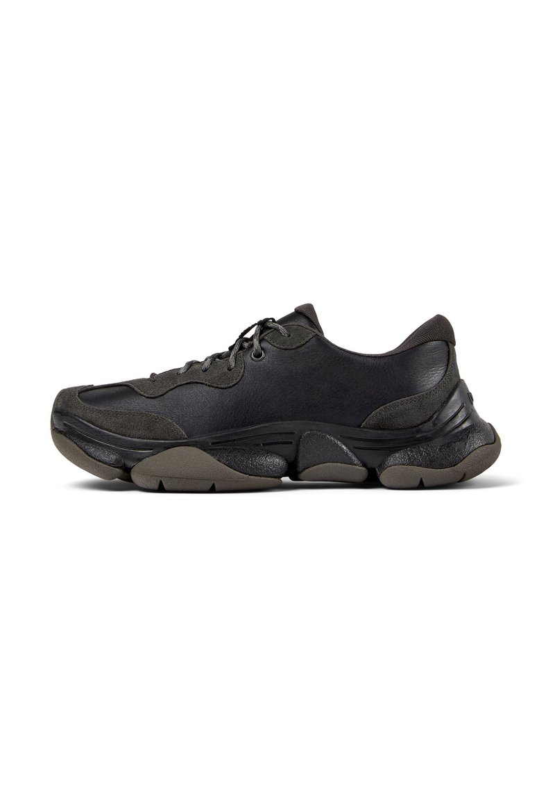 Zwarte sportieve sneaker met een gestructureerde zool, leren en suède bovenwerk, gevoerde kraag en vetersluiting, getoond in zijprofiel.