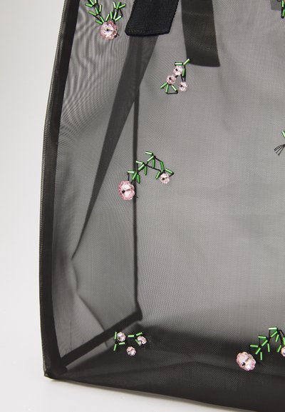 Sort mesh tote taske med broderede lyserøde blomster og grønne stængler, med en tekstureret overflade og en sort båndhank foroven.