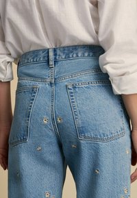 Jeans de mezclilla en azul claro con bordados florales en los bolsillos y en toda la prenda. Diseño de cintura alta con un estilo clásico de cuatro bolsillos.