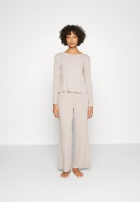 Beige Loungewear-Set mit langärmeligem Crewneck-Oberteil und weit geschnittenen Hosen. Der Stoff hat eine weiche, glatte Textur und eine lockere Passform.